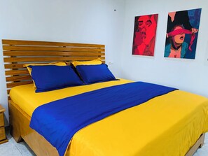 A bed with a wooden headboard, yellow and blue bedding, and two artworks on the wall. - The Penthouse Essentials (Douala)