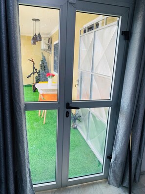 A room with a sliding glass door leading to a green space with a small Christmas tree and a bicycle. - The Penthouse Essentials (Douala)