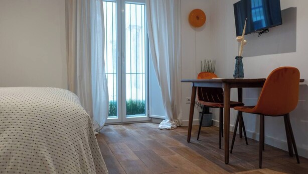 A bedroom with a bed, a desk, a chair, a TV, and a window with curtains. - EL Aljibe Apartments - Ap.5 (Badajoz)