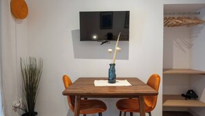 A dining area with a wooden table, two orange chairs, a blue vase with sticks, and a television mounted on the wall. - EL Aljibe Apartments - Ap.5 (Badajoz)