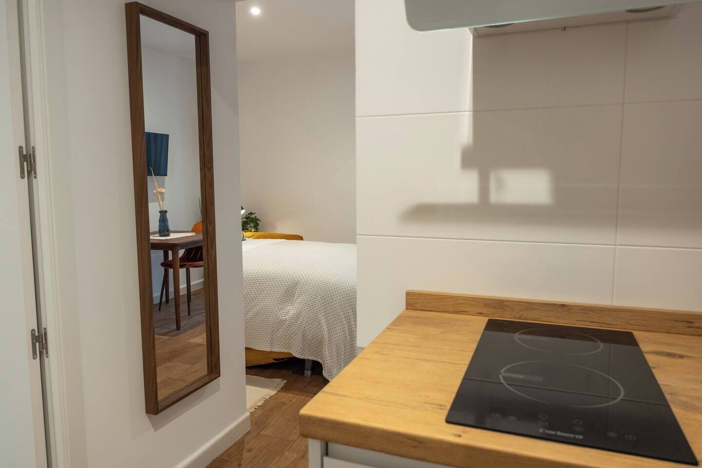 Una cocina compacta con cubierta de madera, placa de inducción negra y salpicadero de azulejos blancos.