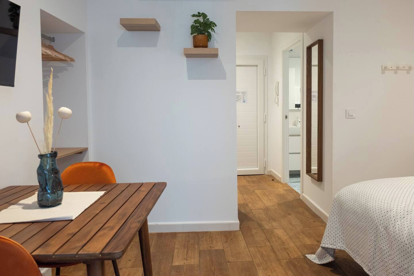 Una habitación moderna con una mesa de comedor de madera, un florero azul con ramas decorativas y una planta en maceta sobre una estantería.