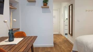Una habitación moderna con una mesa de comedor de madera, un florero azul con ramas decorativas y una planta en maceta sobre una estantería.