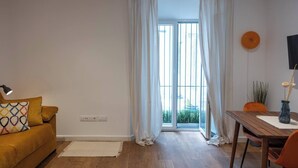 A room with a sofa, a dining table, and a window with curtains. - EL Aljibe Apartments - Ap.5 (Badajoz)