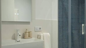 A bathroom with a white sink, mirror, and a glass shower enclosure with blue tiles. - EL Aljibe Apartments - Ap.5 (Badajoz)