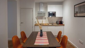 Moderni keittiö, jossa on valkoiset kaapit, ruostumattomasta teräksestä valmistettu mikroaaltouuni ja kahvinkeitin.