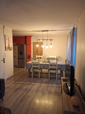 A dining area with a table set for four, a refrigerator in the background, and a television on a stand. - Small house for rent in Lozère near Lac de Naussac Pets welcome (NAUSSAC FONTANES)