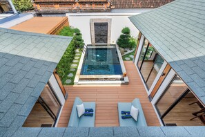 A modern outdoor pool area with a wooden deck, two lounge chairs, and a glass-enclosed hot tub. - Oasis Residences - Serene Sanur Sanctuary, Modern Comfort Meets Nature (Denpasar)