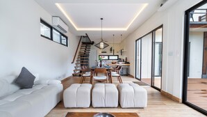 Ein modernes Wohnzimmer mit einer Couch, Hocker, einem Esstisch und einer Treppe.