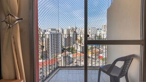 Un balcon donnant sur un paysage urbain, une chaise et un rideau.