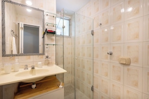 A bathroom with a glass-enclosed shower, a sink with a mirror, and a towel rack.
