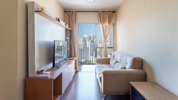 Un salon moderne avec un canapé, un téléviseur posé sur un meuble, une petite table et une fenêtre avec des rideaux.