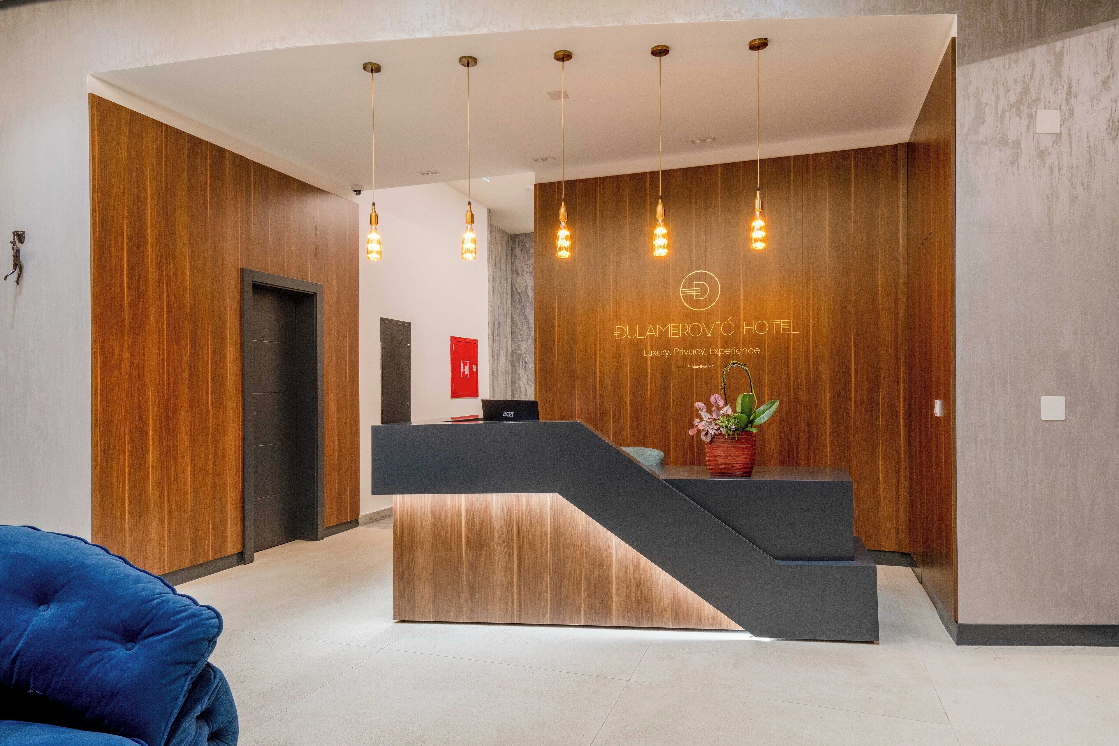 Zona de recepción de hotel con diseño moderno, que incluye un mostrador de madera, una escalera y lámparas colgantes.
