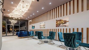 A modern interior with teal chairs and sofas, a glass table, and a unique ceiling light fixture. - Dulamerovic Hotel (Ulcinj)