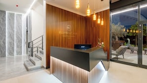 A hotel reception desk with a wooden finish and a digital screen, a staircase, and a view of outdoor seating. - Dulamerovic Hotel (Ulcinj)