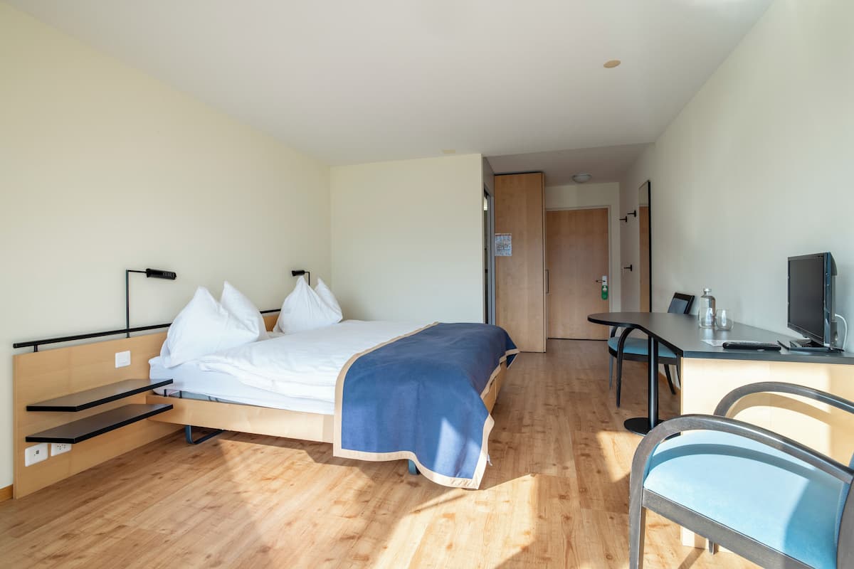 Habitación de hotel con cama, mesitas de noche, un escritorio con silla, televisor y puerta que da a otra habitación.