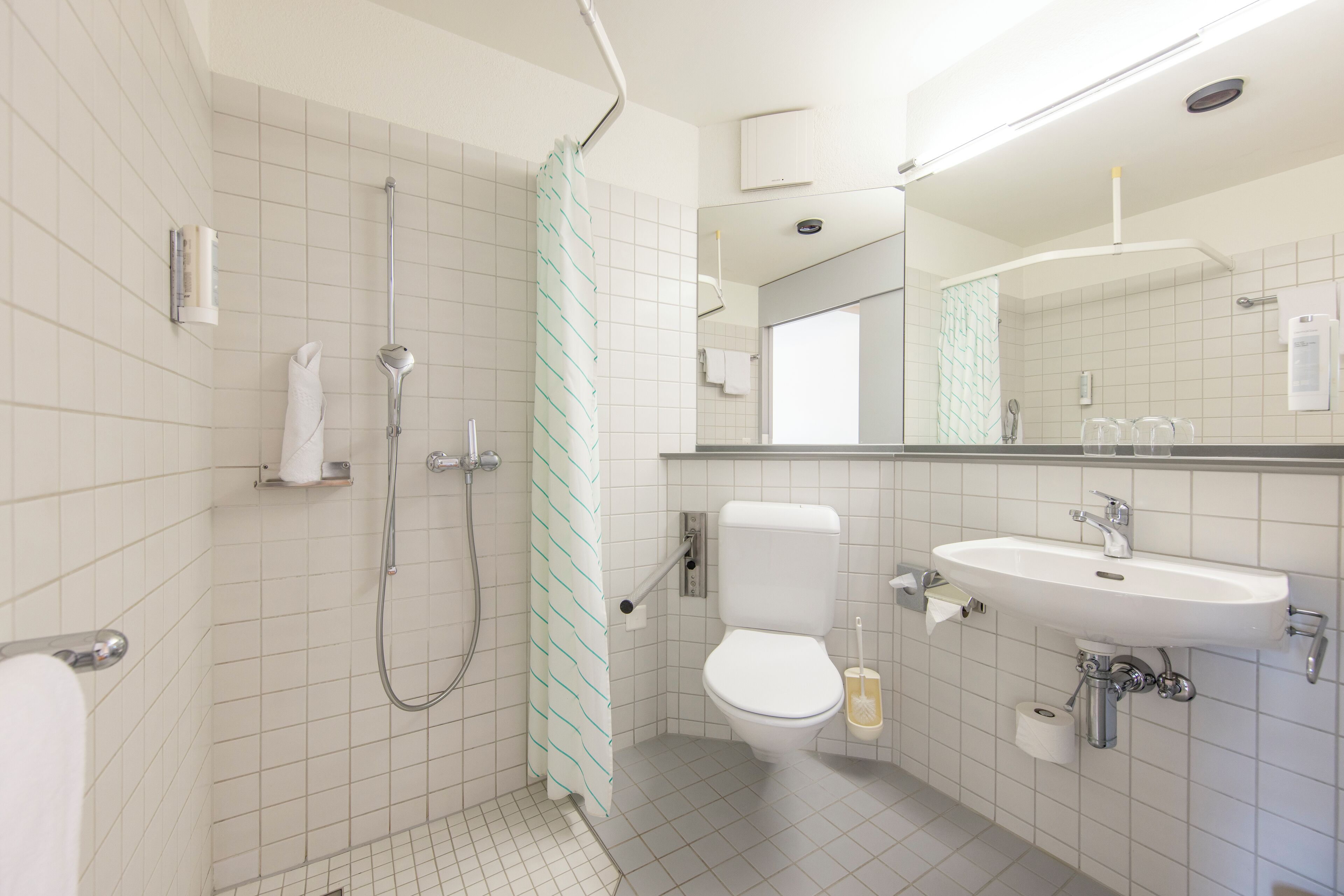 Baño con ducha, inodoro, lavamanos y espejo.