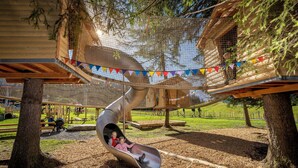 A playground with a slide, netted climbing structures, and a treehouse. - Hotel Panorama (Hasliberg)