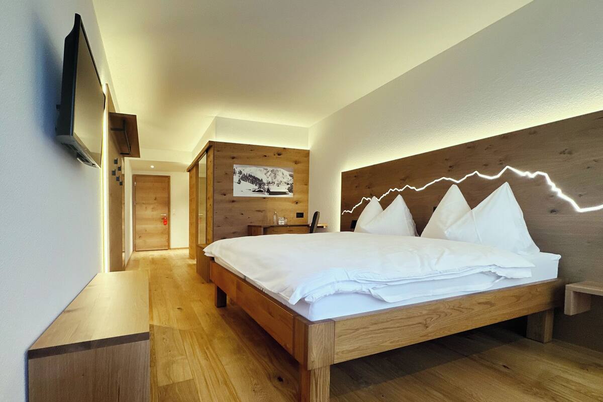 Un dormitorio moderno con cama de madera, televisor montado y cabecera de madera con diseño de montaña.