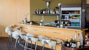 Zona de bar con cabeza de ciervo montada, estantes con varias botellas de licor y taburetes con mantas de piel.