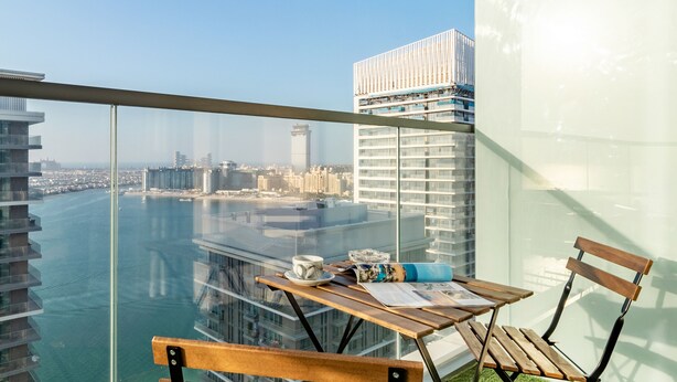 Un balcon avec une table et des chaises, donnant sur un paysage urbain et une étendue d’eau.