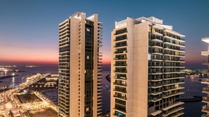Deux immeubles de grande hauteur dotés de nombreux balcons, offrant une vue sur le front de mer et avec un coucher de soleil en arrière-plan.