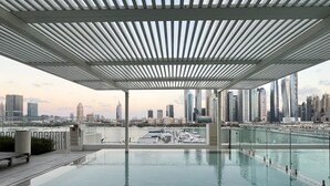 Une piscine à débordement offrant une vue sur le paysage urbain, une architecture moderne et un espace couvert doté d’un toit à lames.