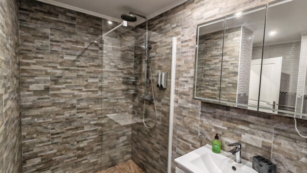 A modern bathroom with a glass-enclosed shower, a white sink with a mirror, and a patterned wall.