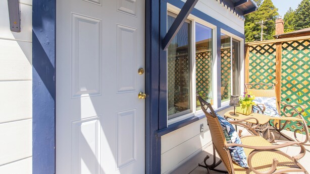 A house with a white door and blue trim, a patio with wicker furniture, and a green lattice fence. - Cottagecore charm beside the redwoods—steps to trails, minutes to beaches and downtown Arcata. (Arcata)