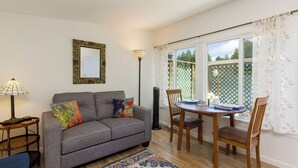 A living room with a grey sofa, a wooden dining table with chairs, a lamp, and a patterned rug. - Cottagecore charm beside the redwoods—steps to trails, minutes to beaches and downtown Arcata. (Arcata)