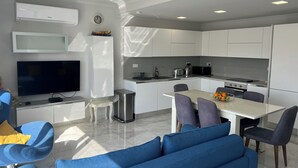 A modern kitchen with white cabinets, a built-in oven, and a dining area with a table and chairs. - Alka Luxury 2 Bedroom Penthouse - Marsalforn (Ix-Xagħra)