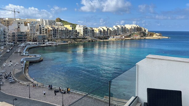 A coastal town with a curved waterfront promenade, buildings along the coast, and a clear blue sky. - Alka Luxury 2 Bedroom Penthouse - Marsalforn (Ix-Xagħra)