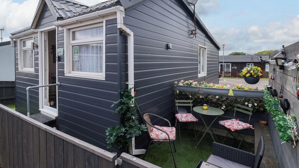 Una casa compacta con fachada oscura, un pequeño patio con mesa y sillas, y un jardín con plantas en macetas.