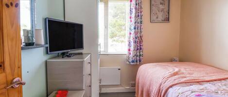 A bedroom with a bed, a TV on a dresser, a window with curtains, and a radiator.