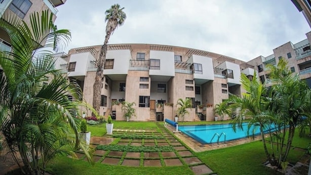 Un edificio moderno con piscina, rodeado de palmeras y un césped cuidado.