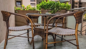 Un conjunto de mesa y sillas de mimbre en un balcón con vistas a un edificio y vegetación.