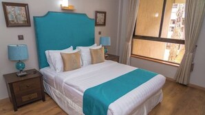 Un dormitorio con una cama grande, dos mesitas de noche con lámparas, una ventana con cortinas y obras de arte en las paredes.