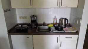 A compact kitchen with white cabinets, a coffee maker, a kettle, and a sink.