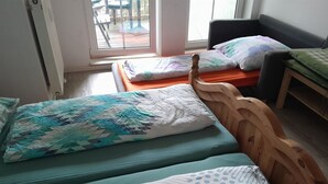 A room with two wooden beds, one with a teal bedspread and the other with a white and blue patterned bedspread. There is a window with a view of an outdoor deck.