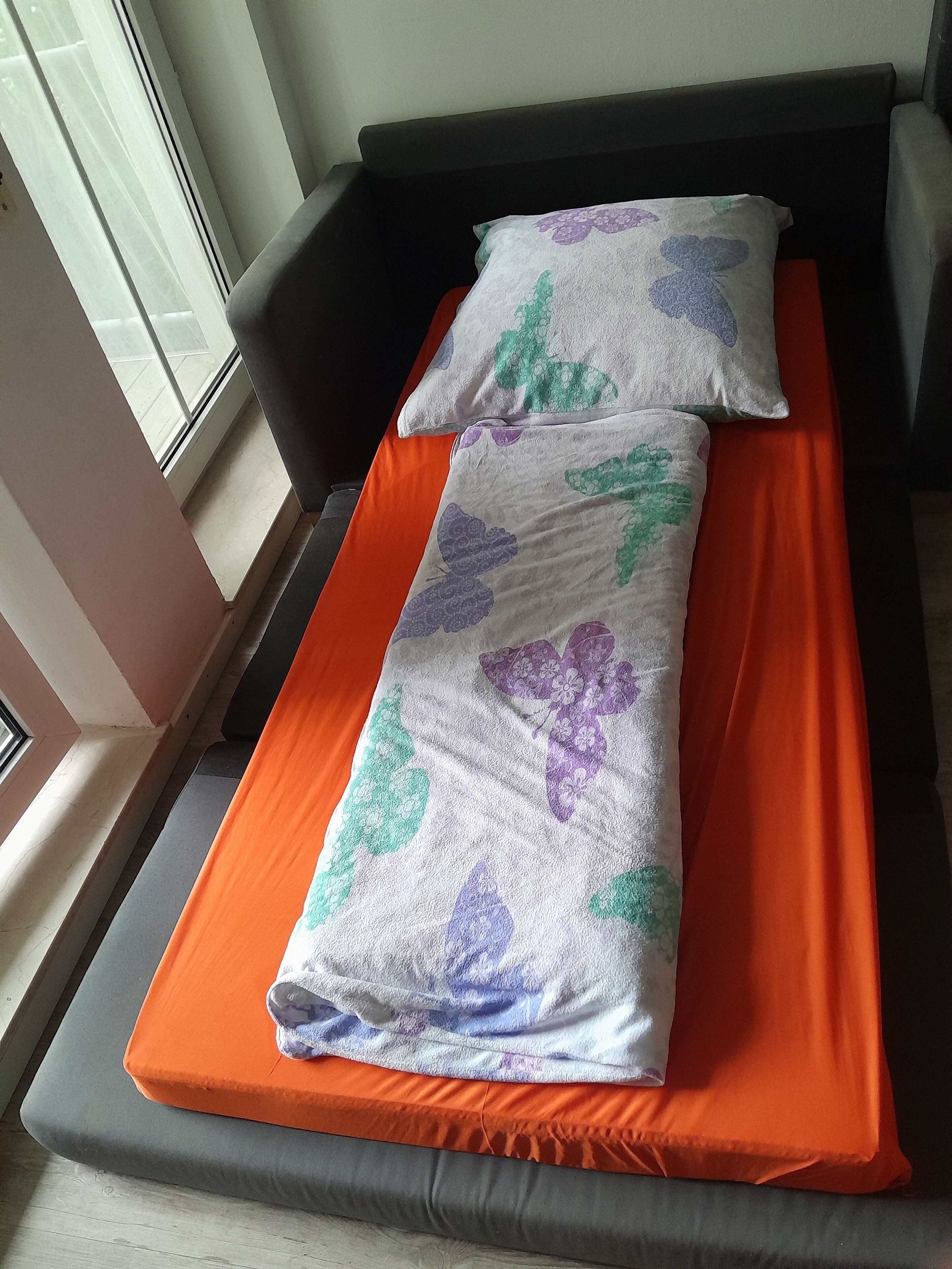 Una cama individual con un colchón naranja y una manta estampada con motivos florales.