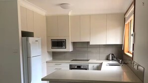A modern kitchen with white cabinets, a built-in microwave, a stainless steel sink, and a bar stool.