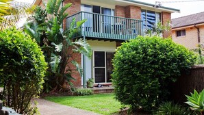 A two-story house with a balcony, surrounded by lush greenery and a well-maintained lawn.