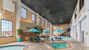 An indoor pool area with multiple pools, seating areas, and umbrellas.