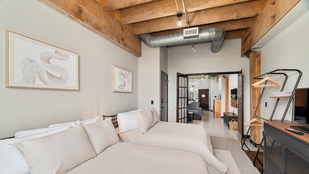 A modern bedroom with two beds, a wooden ceiling, and a hallway leading to a living area.