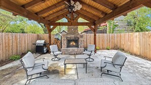 Eine überdachte Terrasse im Freien mit Kamin aus Stein, einer Sitzgruppe und einem Grill.