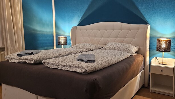 A modern bedroom with a large bed, two bedside tables with lamps, and a blue accent wall.