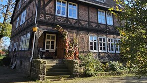A traditional half-timbered house with a steeply pitched roof, multiple windows, and a stone staircase leading to the entrance.