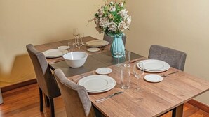 Una mesa de comedor dispuesta con platos, fuentes y cubiertos blancos, acompañada de un florero y un vaso de agua.