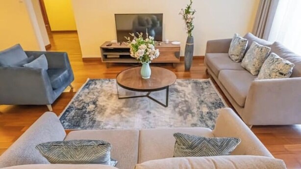 Una sala de estar moderna con un sofá gris, una mesa redonda de centro con un jarrón de flores y un televisor de pantalla plana sobre un soporte de madera.