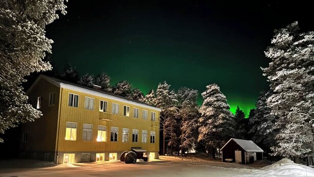 Un edificio di due piani con il terreno innevato, circondato da alberi.